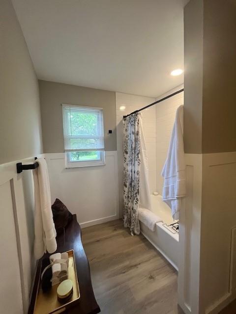 full bathroom featuring wood finished floors, shower / bath combination with curtain, and a wainscoted wall