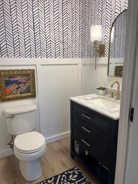 half bathroom with wood finished floors, toilet, and vanity