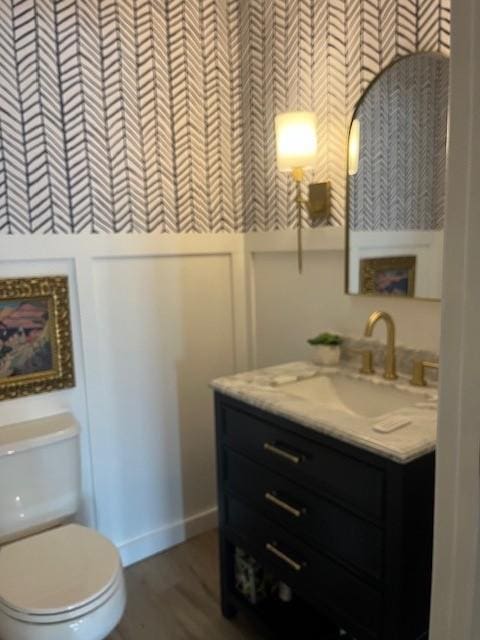 bathroom with toilet, vanity, wood finished floors, and baseboards