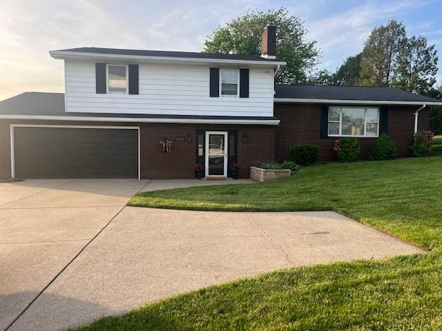 tri-level home with a chimney, driveway, brick siding, and a front lawn