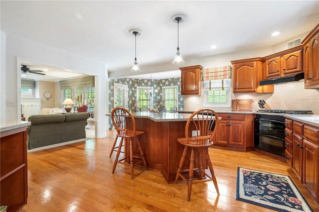 kitchen featuring stove, a breakfast bar area, under cabinet range hood, light wood-style flooring, and hanging light fixtures
