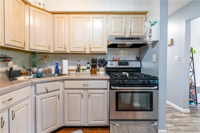 kitchen with stainless steel gas range oven, under cabinet range hood, a sink, backsplash, and light countertops