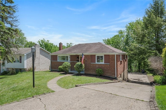 view of front of home featuring brick siding, driveway, a front yard, and a chimney