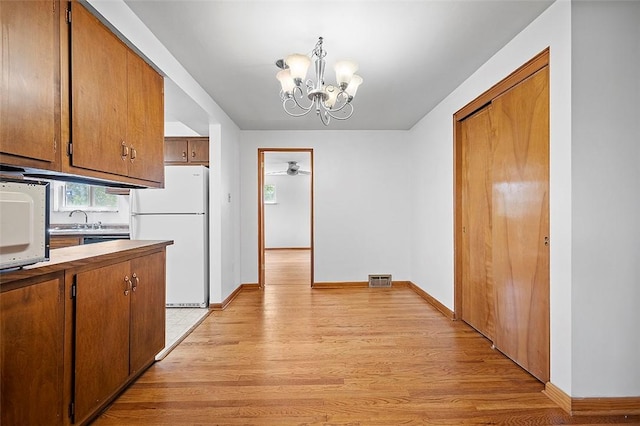 kitchen with white appliances, light wood-type flooring, brown cabinets, and a chandelier