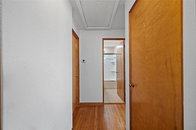 hallway featuring attic access, wood finished floors, and baseboards