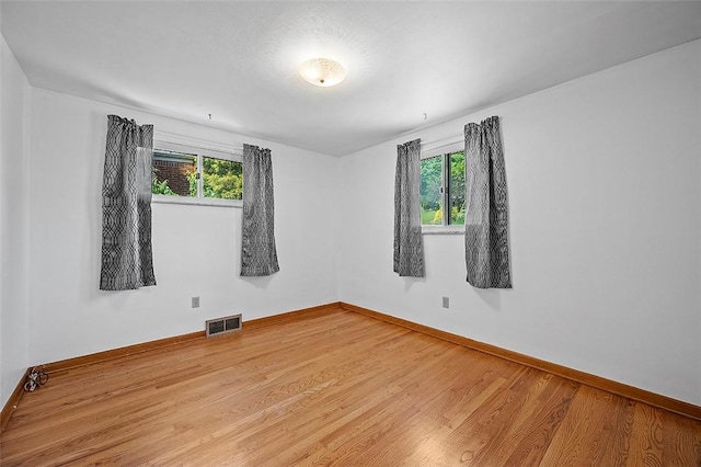 empty room featuring healthy amount of natural light, baseboards, and wood finished floors