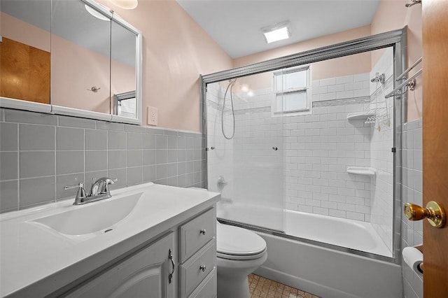 full bath with toilet, shower / bath combination with glass door, tile walls, vanity, and wainscoting