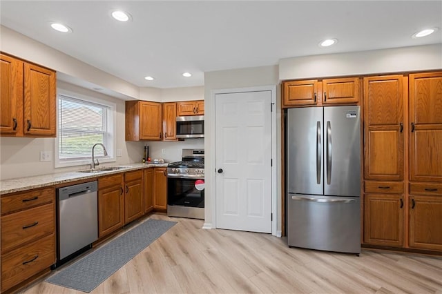 kitchen with appliances with stainless steel finishes, a sink, brown cabinetry, light wood-style floors, and recessed lighting