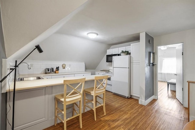 kitchen featuring white appliances, a sink, light wood finished floors, a peninsula, and vaulted ceiling