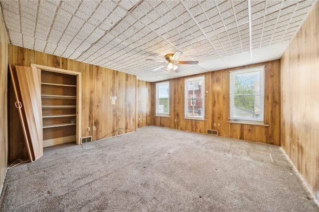 unfurnished room with plenty of natural light, ceiling fan, wood walls, and carpet flooring