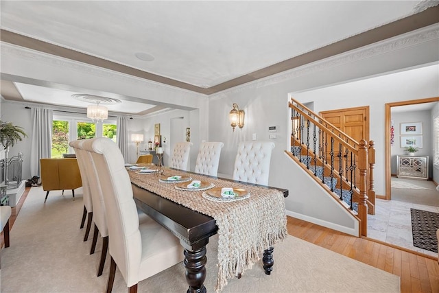 dining area featuring light wood-style floors, stairway, crown molding, baseboards, and a raised ceiling