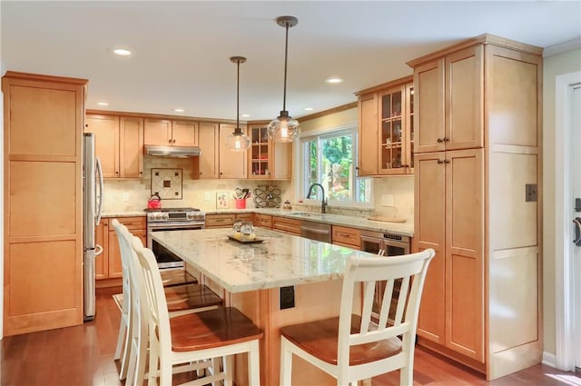 kitchen with stainless steel appliances, a sink, under cabinet range hood, a center island, and a breakfast bar area