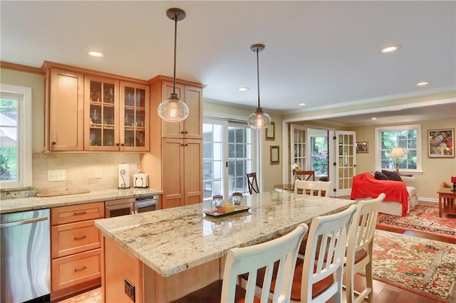kitchen featuring stainless steel dishwasher, open floor plan, a breakfast bar area, ornamental molding, and glass insert cabinets