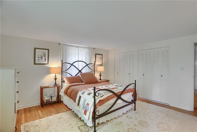 bedroom with two closets, light wood-type flooring, and baseboards