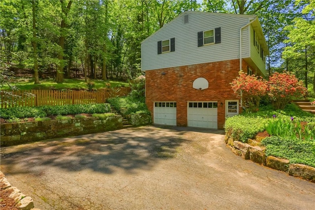 view of property exterior featuring an attached garage, driveway, brick siding, and fence