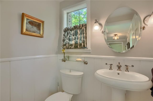 half bathroom with wainscoting, toilet, and a sink
