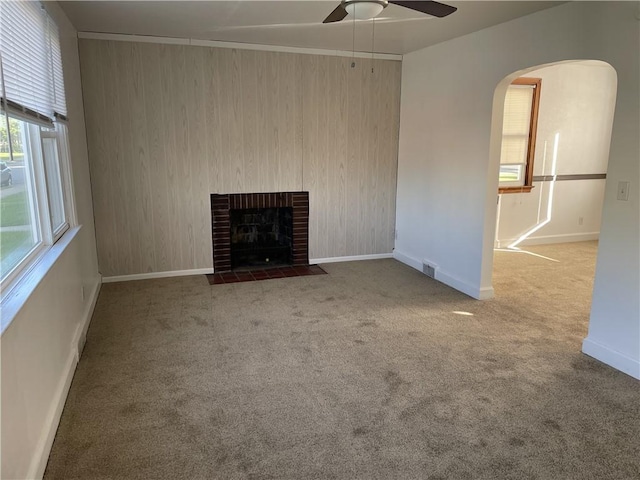 unfurnished living room with ceiling fan, arched walkways, carpet floors, baseboards, and a brick fireplace