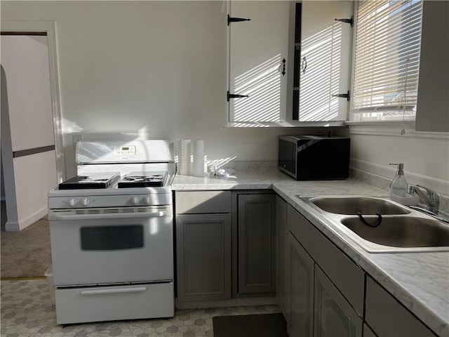 kitchen with white gas range oven, a sink, light countertops, and gray cabinetry