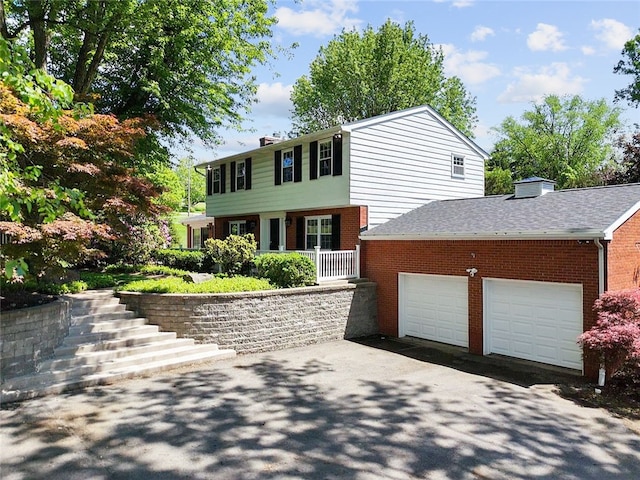 colonial home with a chimney, brick siding, driveway, and an attached garage