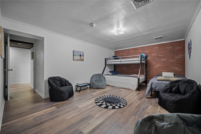 bedroom with wood finished floors, baseboards, ornamental molding, and brick wall