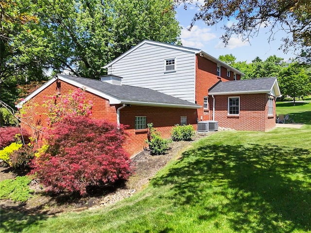rear view of house with brick siding, a lawn, and roof with shingles