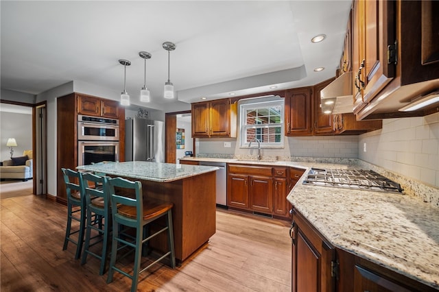 kitchen with a sink, stainless steel appliances, a kitchen bar, a center island, and light wood-style flooring