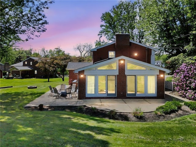 rear view of house with a patio, a lawn, a chimney, and brick siding