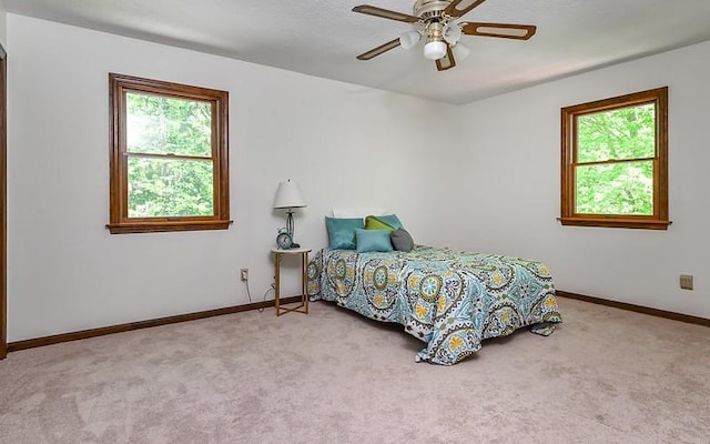 carpeted bedroom featuring multiple windows, baseboards, and ceiling fan