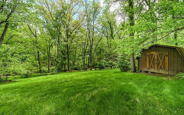 view of green lawn with a storage unit, an outbuilding, and a wooded view