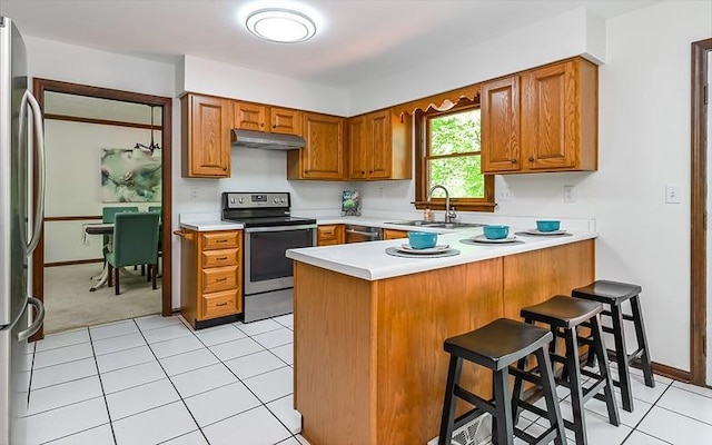 kitchen featuring stainless steel appliances, a sink, under cabinet range hood, a peninsula, and light countertops