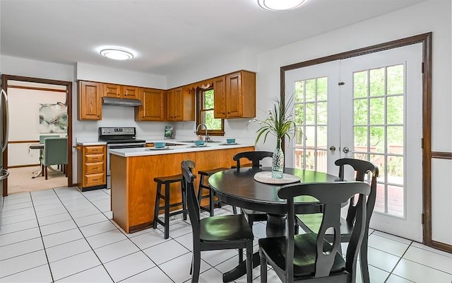 kitchen featuring stainless steel range with electric stovetop, under cabinet range hood, light countertops, a peninsula, and brown cabinets
