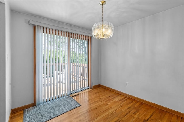 empty room featuring a chandelier, baseboards, and wood finished floors