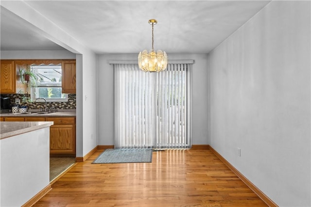 unfurnished dining area featuring a chandelier, a sink, light wood-style flooring, and baseboards