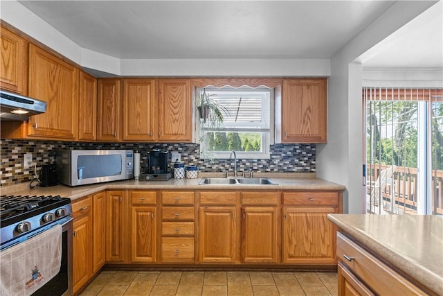 kitchen with appliances with stainless steel finishes, a sink, under cabinet range hood, light countertops, and backsplash