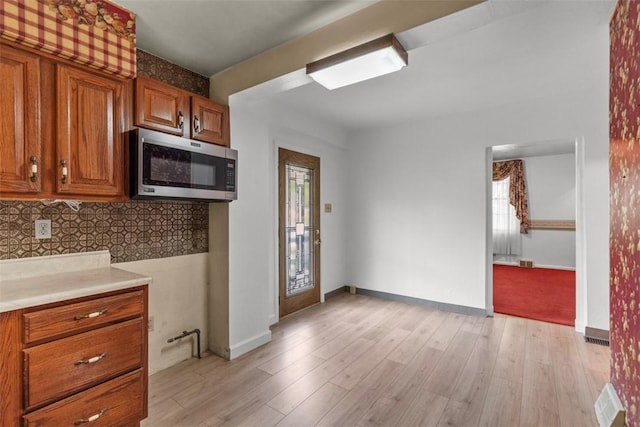 kitchen with stainless steel microwave, brown cabinetry, tasteful backsplash, light wood-type flooring, and light countertops