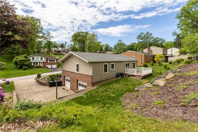 rear view of property with a garage, concrete driveway, a wooden deck, brick siding, and a yard