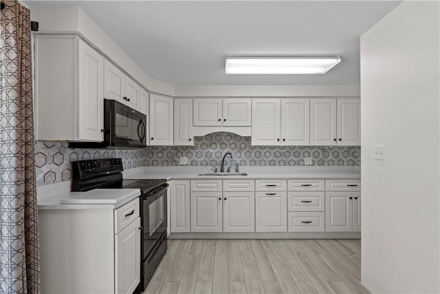 kitchen featuring black appliances, a sink, light countertops, white cabinets, and light wood-type flooring