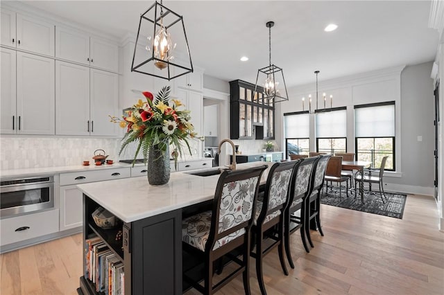 kitchen with a sink, a chandelier, backsplash, light wood-type flooring, and open shelves