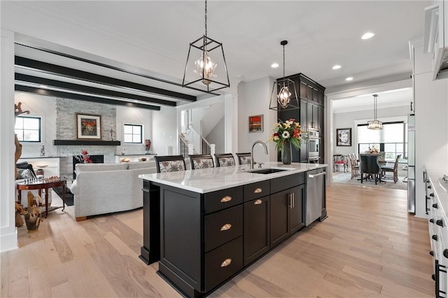 kitchen with a sink, appliances with stainless steel finishes, light wood-type flooring, a kitchen island with sink, and hanging light fixtures