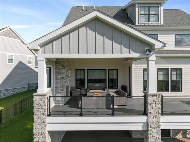 rear view of house featuring board and batten siding, an outdoor living space, a shingled roof, and stone siding