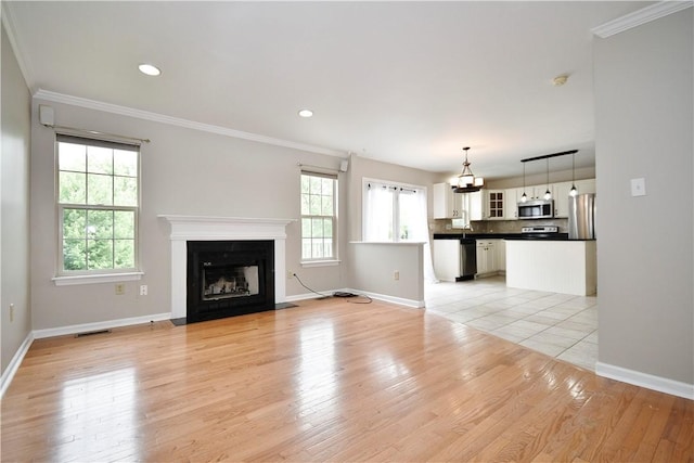 unfurnished living room featuring baseboards, crown molding, light wood finished floors, a fireplace with flush hearth, and a chandelier