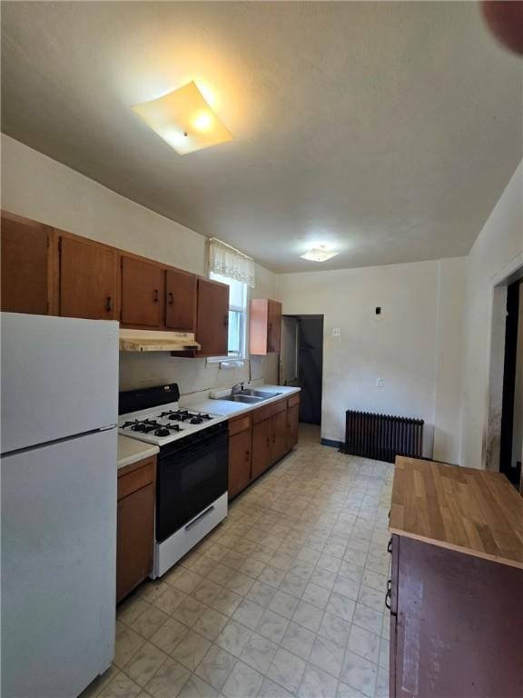 kitchen with freestanding refrigerator, range with gas cooktop, under cabinet range hood, radiator heating unit, and light countertops