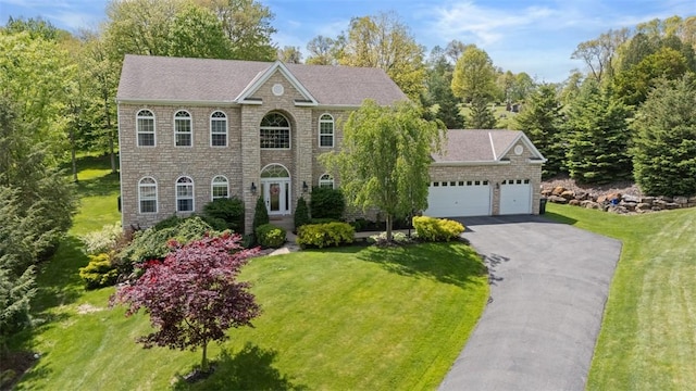georgian-style home with an attached garage, driveway, stone siding, and a front lawn