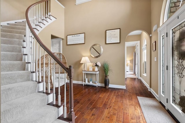 foyer featuring hardwood / wood-style floors, arched walkways, stairway, baseboards, and a towering ceiling