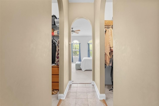 hall featuring arched walkways, light tile patterned flooring, and baseboards