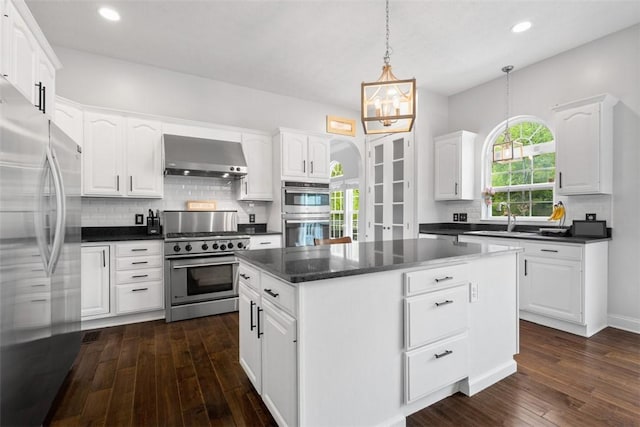 kitchen with appliances with stainless steel finishes, dark countertops, wall chimney range hood, a center island, and recessed lighting