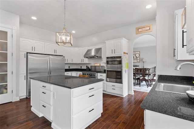 kitchen with wall chimney range hood, a sink, appliances with stainless steel finishes, dark wood finished floors, and recessed lighting