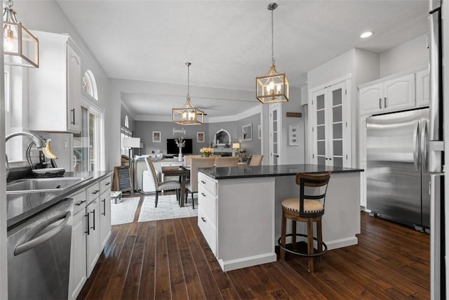 kitchen with stainless steel appliances, a sink, dark countertops, white cabinetry, and a chandelier