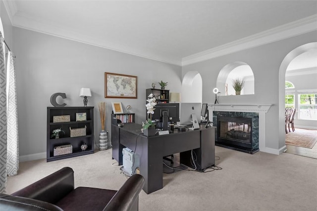carpeted office space with crown molding, a premium fireplace, arched walkways, and baseboards