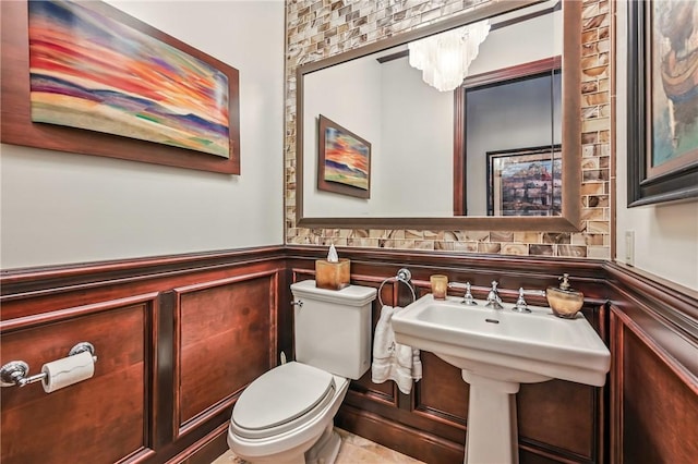 bathroom featuring a wainscoted wall, toilet, and a chandelier
